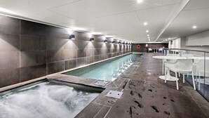 A modern indoor swimming pool with a long, narrow design, surrounded by dark tiled walls and white ceiling lights. - Bright Inner-north Stay With Pool Access (Melbourne)