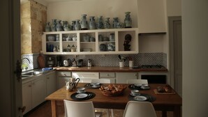 Une cuisine avec des meubles blancs, une table à manger en bois dressée pour quatre personnes, et une étagère au-dessus du comptoir où sont exposées diverses assiettes en céramique bleue et blanche.