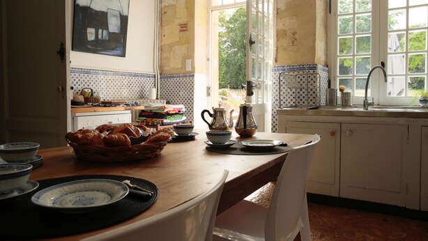 Une cuisine avec une table en bois mise pour le petit-déjeuner, un évier et une fenêtre donnant sur un paysage verdoyant.