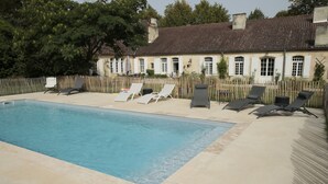 Une piscine rectangulaire, dotée de chaises longues et entourée d’une clôture en bois.