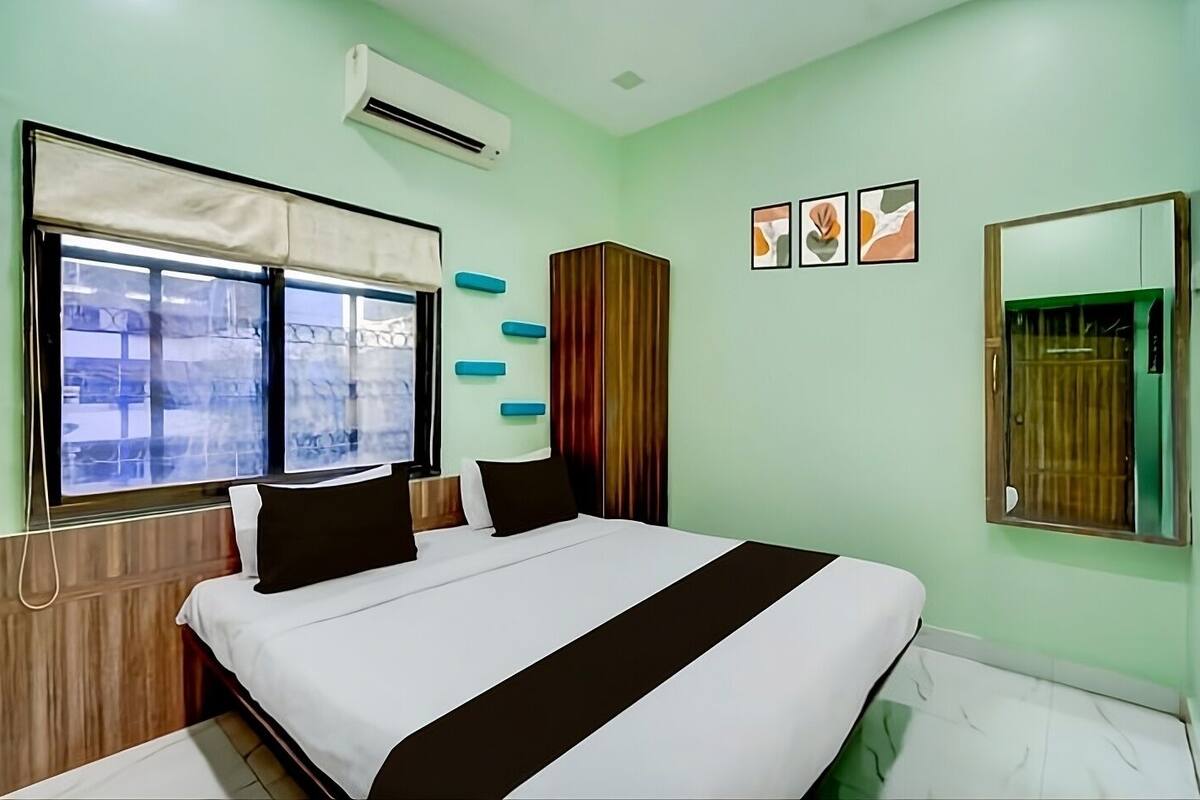 A hotel room with a large bed, a window with a view, an air conditioner, and a mirror.