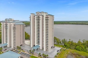 A high-rise residential building with multiple balconies, a parking area, and a view of a large body of water. - Nice cozy Lake condo, Disney & NASA launches view! (Orlando)