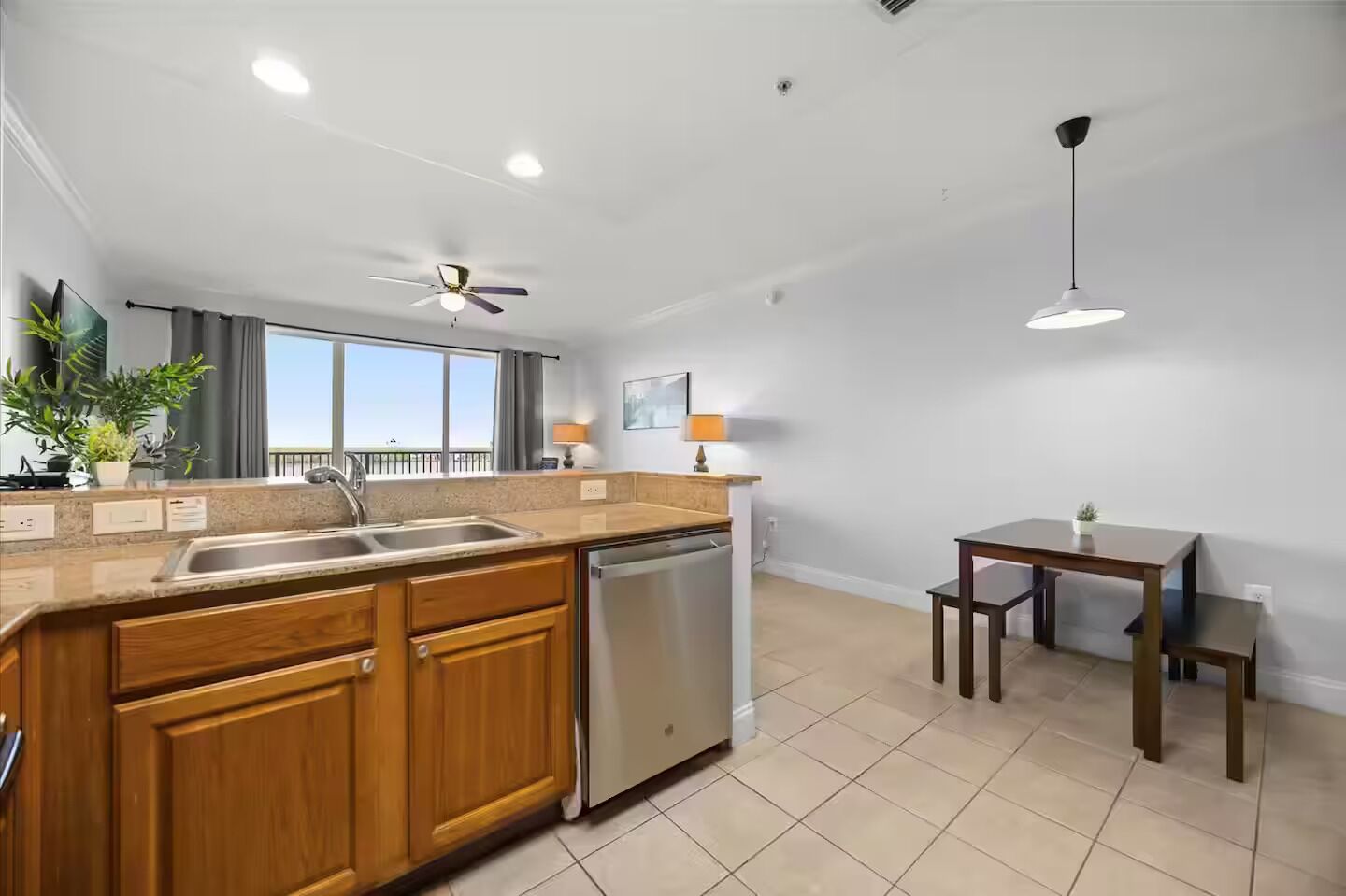 A modern kitchen with wooden cabinets, a stainless steel dishwasher, and a dining area with a table and chairs.