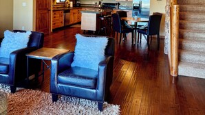 Un espacio habitable amplio con techo alto, vigas de madera, chimenea central y una distribución acogedora con dos sofás de cuero y una alfombra mullida.