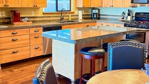 Una cocina con armarios de madera, encimera de granito, estufa integrada y comedor con mesa redonda y sillas.