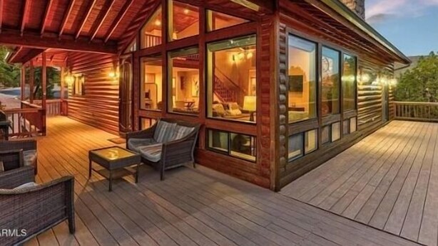 Una cabaña de troncos con terraza, ventanas grandes y un patio cubierto.