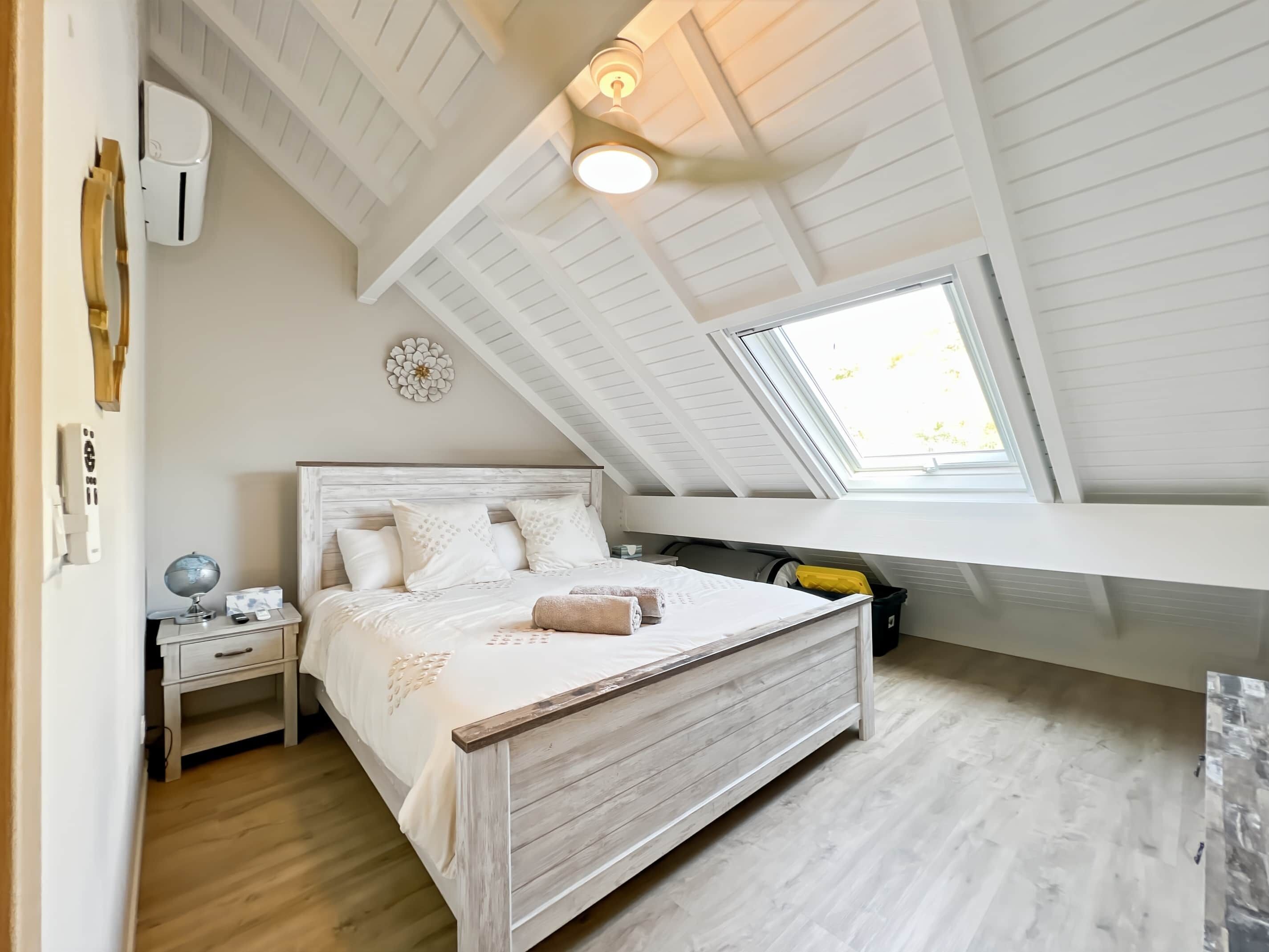 Quarto com teto inclinado, claraboia, estrutura de cama de madeira, mesa de cabeceira com abajur e um globo.