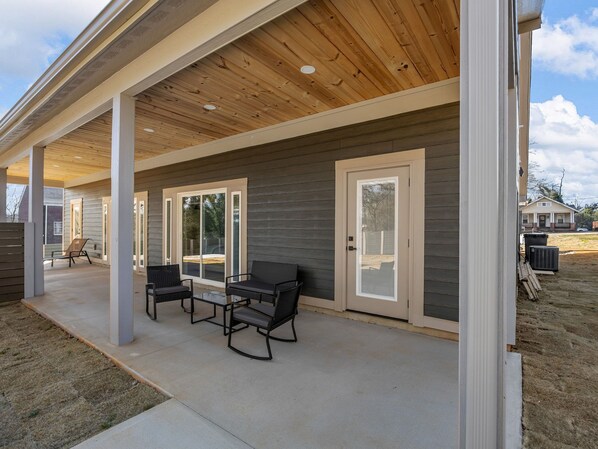 A covered patio area with a concrete floor, two black chairs, and a table.