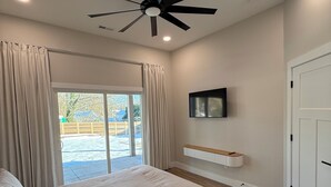 Une chambre dotée d’un grand lit, d’un ventilateur de plafond, d’un téléviseur fixé au mur et d’une porte-fenêtre coulissante donnant sur une terrasse.
