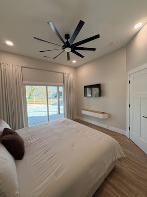 A bedroom with a large bed, a ceiling fan, a TV mounted on the wall, and a sliding glass door leading to a patio. - Spartanburg Convenience (Spartanburg)