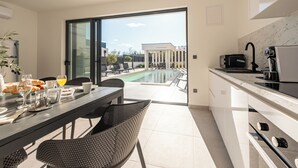 Une cuisine moderne avec un coin repas, une vue sur une piscine et une porte-fenêtre coulissante.