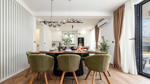 Un espace de repas moderne avec une table en bois et trois chaises vertes, un lustre et une vue sur l’extérieur.