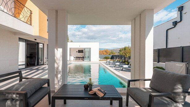 Une terrasse extérieure moderne avec une piscine, des sièges et une vue sur un bâtiment en arrière-plan.