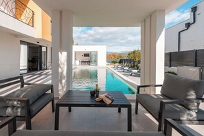 A modern outdoor patio with a pool, seating, and a view of a building in the background. - Luxury Villa- FOR GIFT (Pridraga)