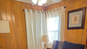 A bedroom with a large bed, wooden walls, a ceiling fan, and a window with curtains. - Open Lakeview Cottage #5 at Teal Point Resort on Lake Norfork (Mountain Home)