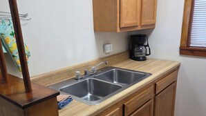 A small kitchen with wooden cabinets, a double sink, and a coffee maker. - Open Lakeview Cottage #5 at Teal Point Resort on Lake Norfork (Mountain Home)