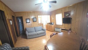 A wooden-paneled room with a sofa, a dining table with chairs, a ceiling fan, and a television mounted on the wall. - Open Lakeview Cottage #5 at Teal Point Resort on Lake Norfork (Mountain Home)