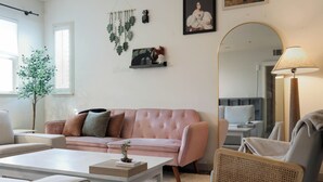 Ein Wohnzimmer mit einem rosa Sofa, einem weißen Couchtisch, einem Rattankorbstuhl und einem großen Spiegel.