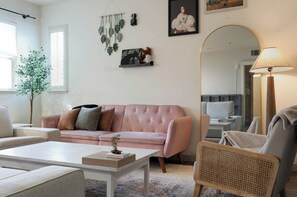 Een woonkamer met een roze bank, een witte salontafel, een rieten stoel en een spiegel.