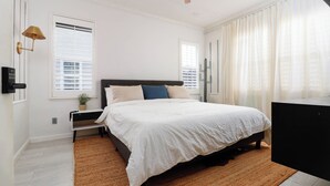 Ein Schlafzimmer mit einem Bett, Deckenventilator, Nachttisch mit Lampe und einem Fenster mit Jalousien.