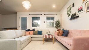 Ein Wohnzimmer mit einem beigefarbenen Ecksofa, einem rosafarbenen Sofa, einem Couchtisch und einem weißen Teppich.