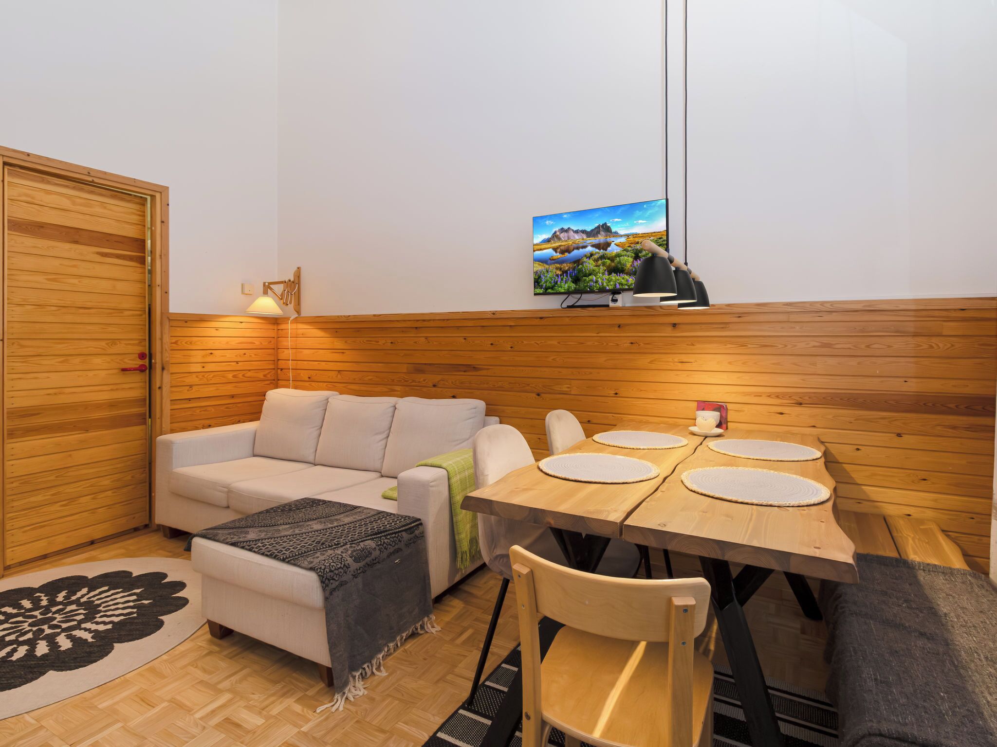 Une pièce chaleureuse avec un mur en bois, un canapé, une table à manger avec des chaises et un téléviseur fixé au mur.