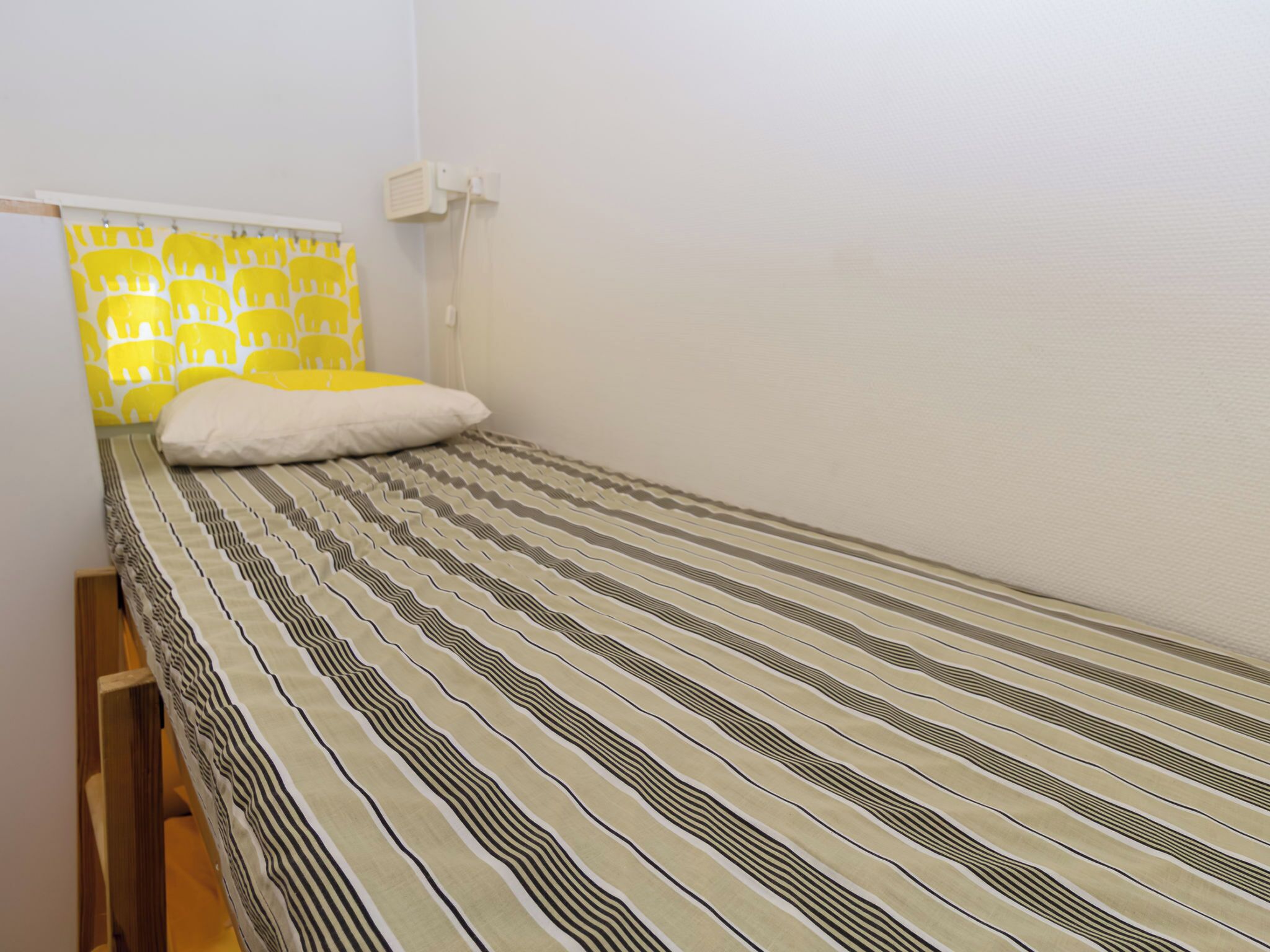 Una cama individual con una colcha a rayas, una almohada blanca y un cabecero con estampado de elefantes.