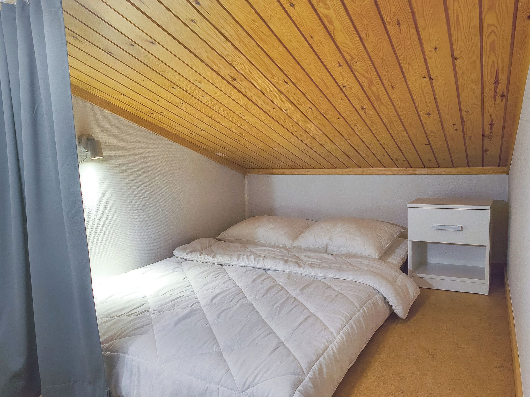 Une petite chambre avec un lit simple, un plafond en bois, une table de chevet et une commode.