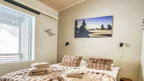 A bedroom with a large bed, a window with blinds, a painting on the wall, and a small stool. - Pikkuhippu by Interhome (Pelkosenniemi)
