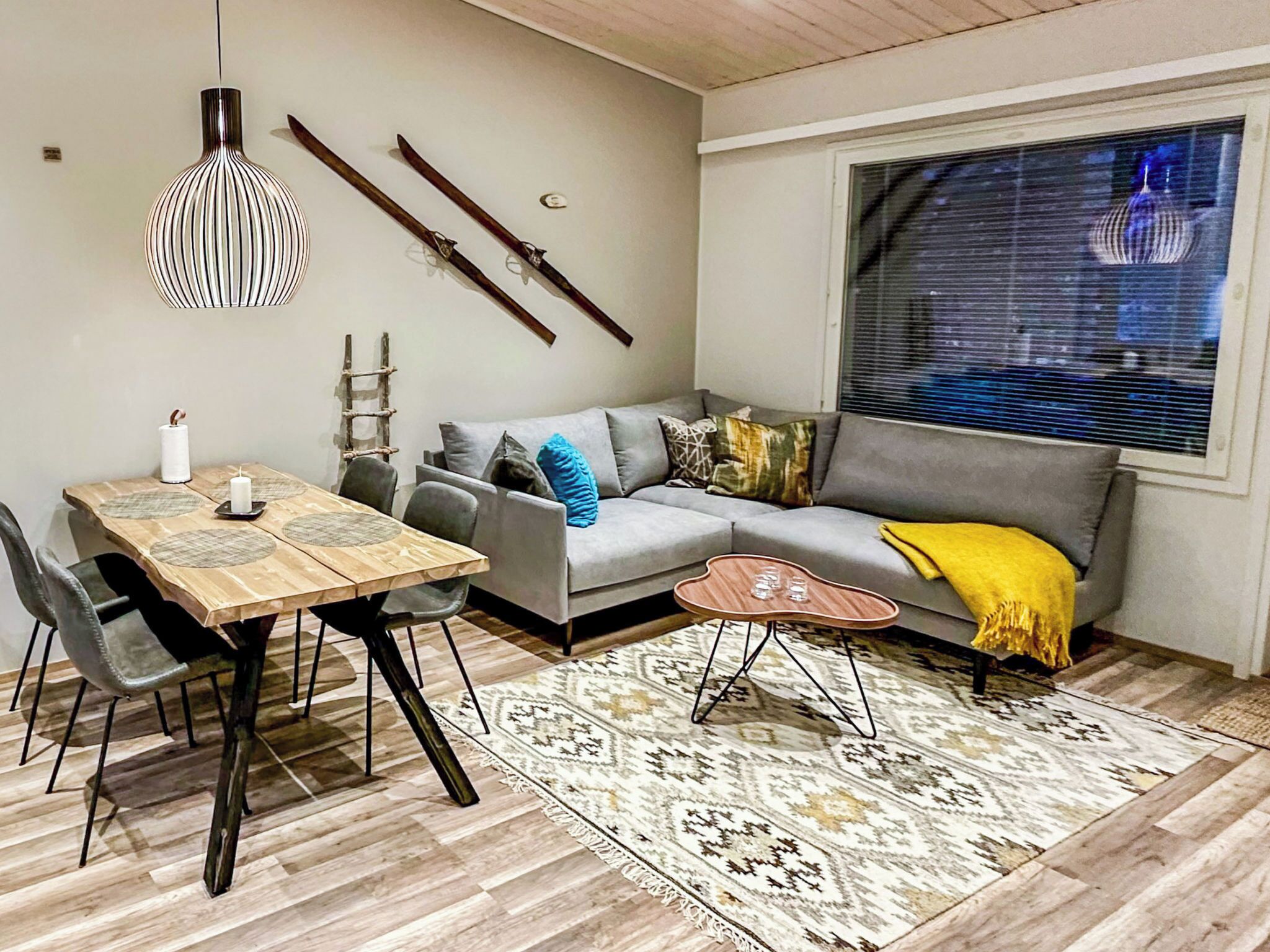 A modern living room with a wooden dining table, grey sofa, and a patterned rug.