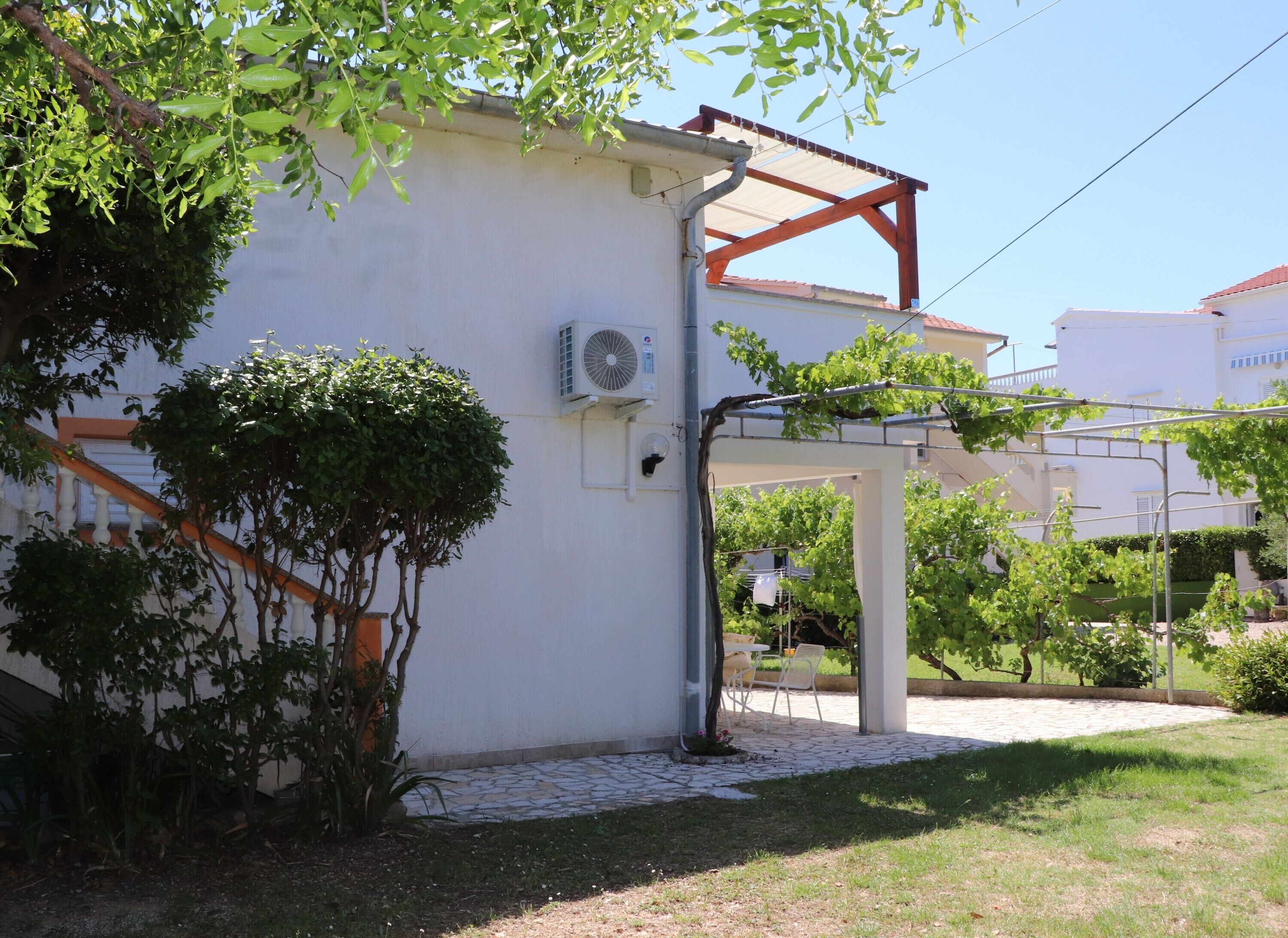 A building with a white exterior, a covered outdoor area with a pergola, and a stone pathway leading to the entrance.