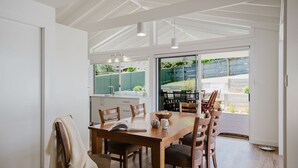 Een moderne keuken met een grote eettafel, houten stoelen en uitzicht op de achtertuin door grote ramen.