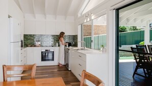 Een moderne keuken met witte kasten, een tegelwand van baksteen en een groot raam met uitzicht op een terras.