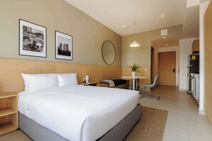 A modern hotel room with a large bed, a desk, a chair, a small table with a plant, and a kitchenette. - w* | Deluxe Loft w/ Balcony in Tabacalera (Ciudad de México)