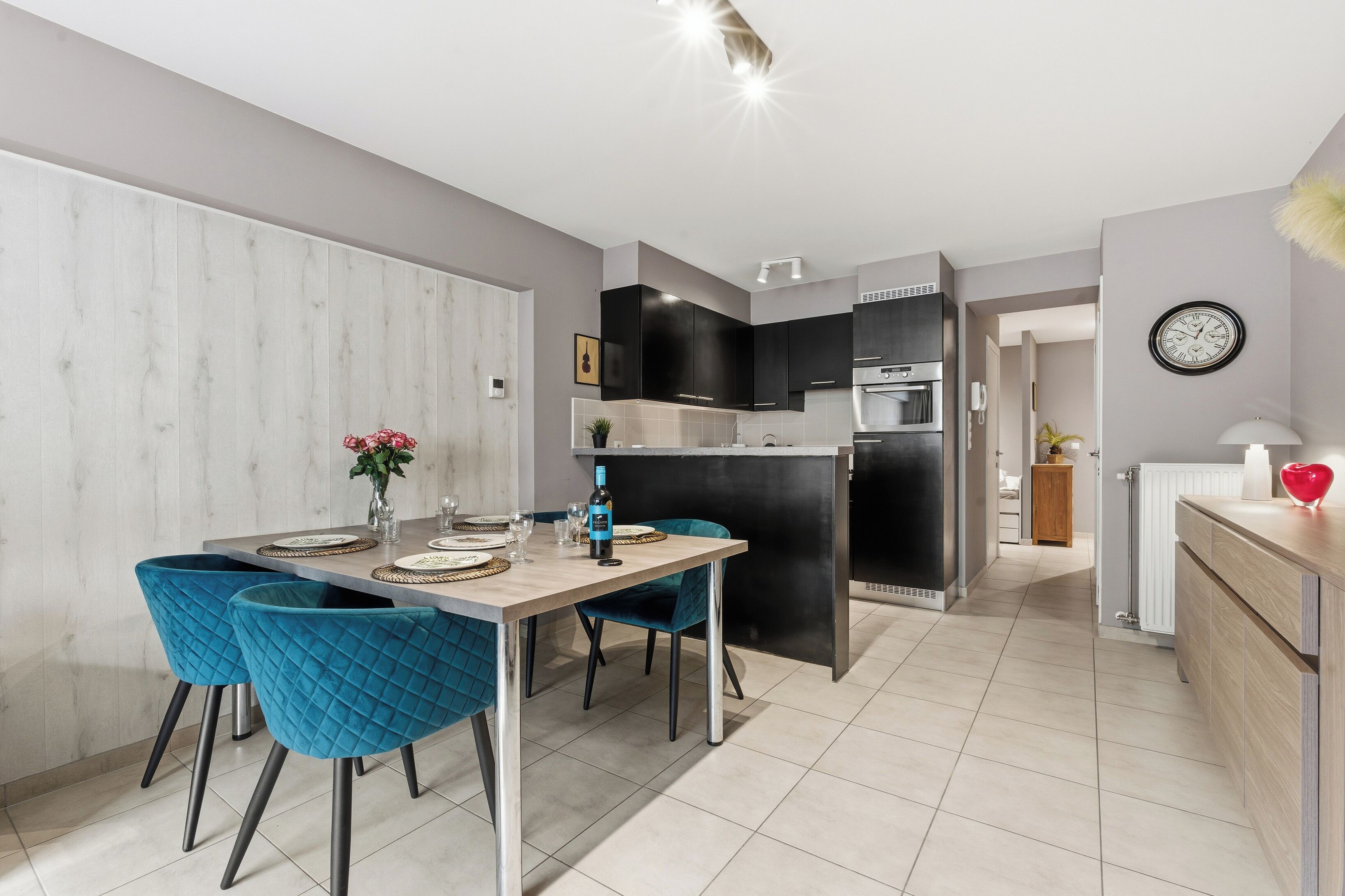 A modern kitchen with black cabinets, a central island, and a dining area with blue chairs.