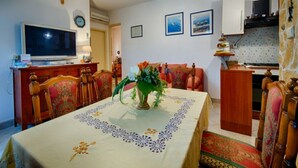 Uma sala de jantar com uma mesa posta para quatro pessoas, uma televisão e um ventilador de teto.