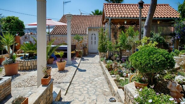 A courtyard with a stone pathway, potted plants, and a building with a tiled roof. - Golden Coast Apartments - A2 - OneBedroom Apartment with Terrace and SeaView (Vis)