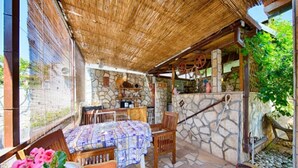 A cozy outdoor seating area with a stone wall, a thatched roof, and a rustic wooden table. - Golden Coast Apartments - A2 - OneBedroom Apartment with Terrace and SeaView (Vis)