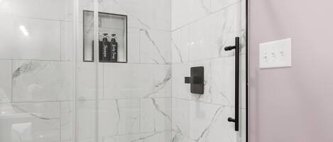 A glass-enclosed shower with a marble-tiled floor and a showerhead mounted on the wall.