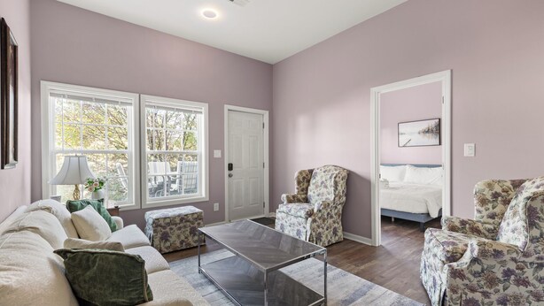A living room with a sofa, armchairs, a coffee table, and a bed. There are large windows and a door leading to another room. - Cozy Garden-Level Retreat 3 Queen Beds (Raleigh)