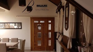 Uma sala de jantar com mesa e cadeiras de madeira, uma porta de madeira com painéis de vidro e uma placa com a inscrição "BELAJEC Winery & Holiday House".