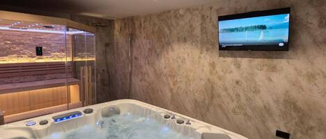 A spa room with a hot tub, a glass-enclosed seating area, and a television mounted on the wall.