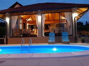 A swimming pool with lounge chairs and a covered outdoor area with a dining setup.