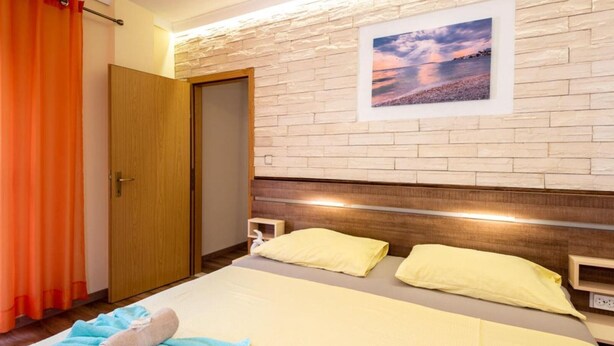 Una habitación de hotel con cama, cabecero de madera, pared de piedra y una pintura de un atardecer.