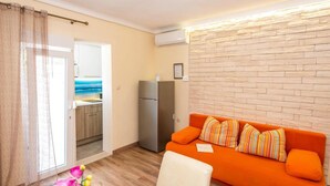 Un espacio habitable compacto con kitchenette, un sofá con cojines a rayas y una zona de comedor con mesa lista para dos personas.