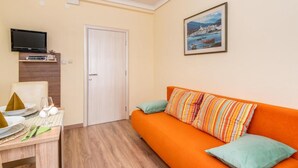 A room with a wooden dining table set for two, a sofa with striped cushions, a television mounted on the wall, and a door. - Villa Goldfield - One Bedroom Apartment with Balcony (Gradac)