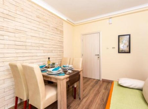 A small dining area with a wooden table set for two, a white door, and a framed picture on the wall.