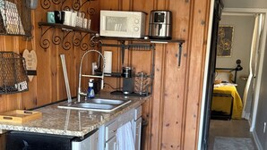 A compact kitchen with a microwave, coffee maker, and a sink. There is a wooden cabinet and a small countertop. - Quaint container home on private road 1bd/1bath that can sleep 4 (Wilmington)