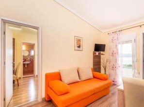 A bright living room with a wooden floor, a bright orange sofa, and a television on a wooden stand. - Villa Goldfield - Superior One Bedroom Apartment with Sea View and Balcony (Gradac)