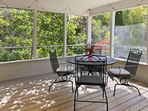 Eine überdachte Terrasse mit einem runden Tisch und vier Stühlen, großen Fenstern und Blick auf Grünflächen.